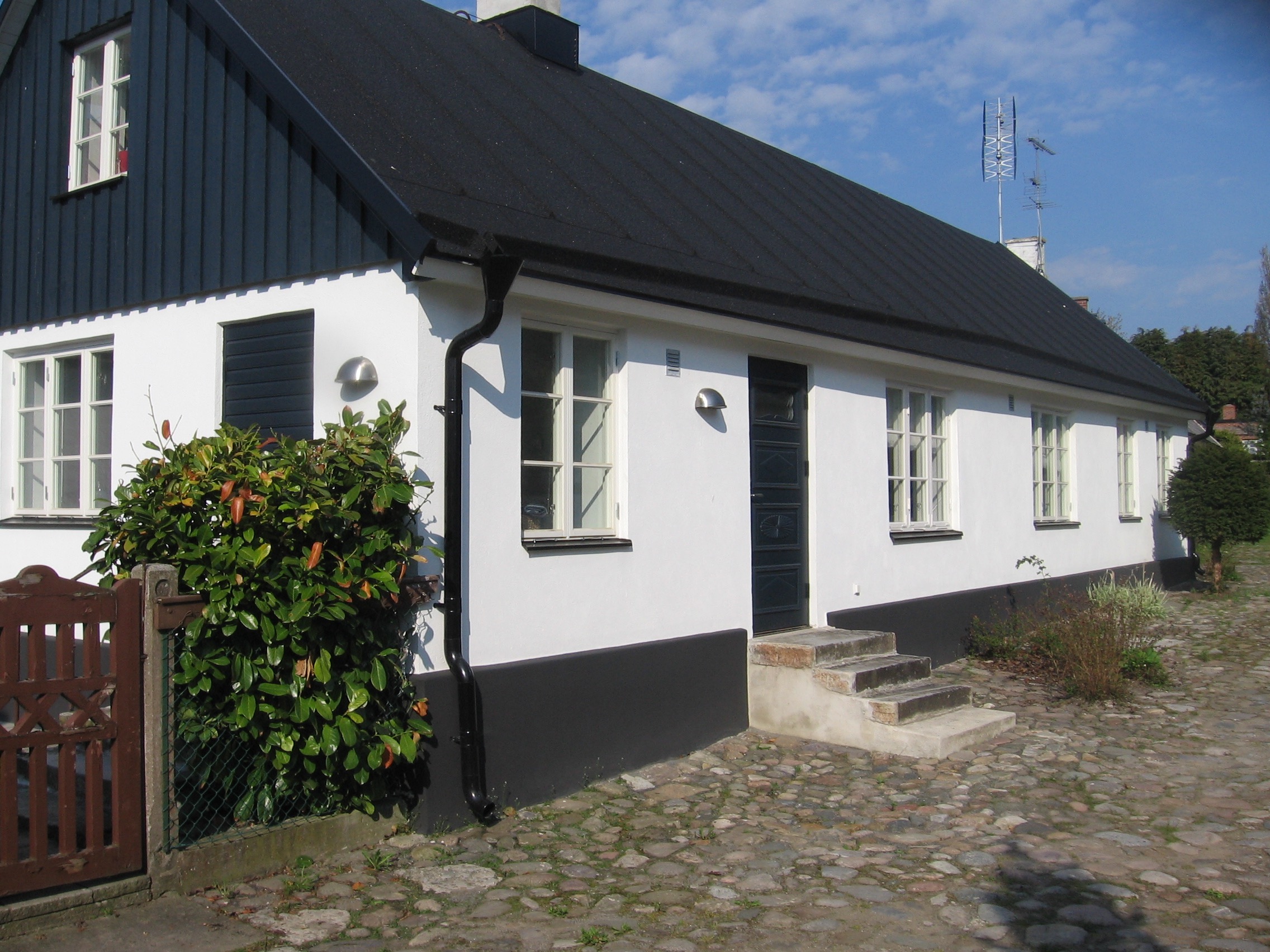 Utvändig målning av litet byhus med fasad, trägavel, grund fönster och dörrar - referens måleriföretaget Gårdbolaget på Österlen